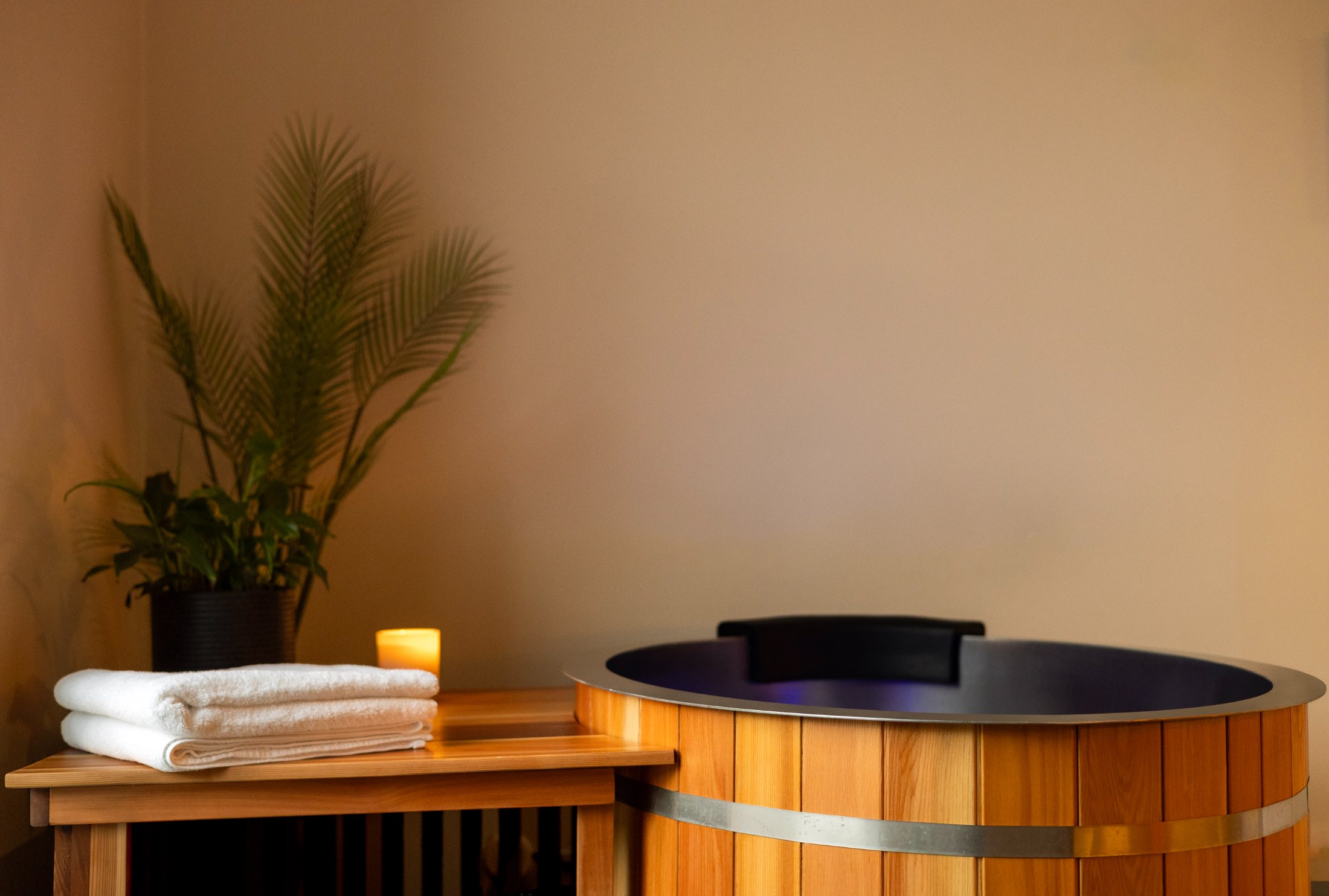 Cedar cold plunge tub with folded towels and a candle in a Sauna Sanctuary room