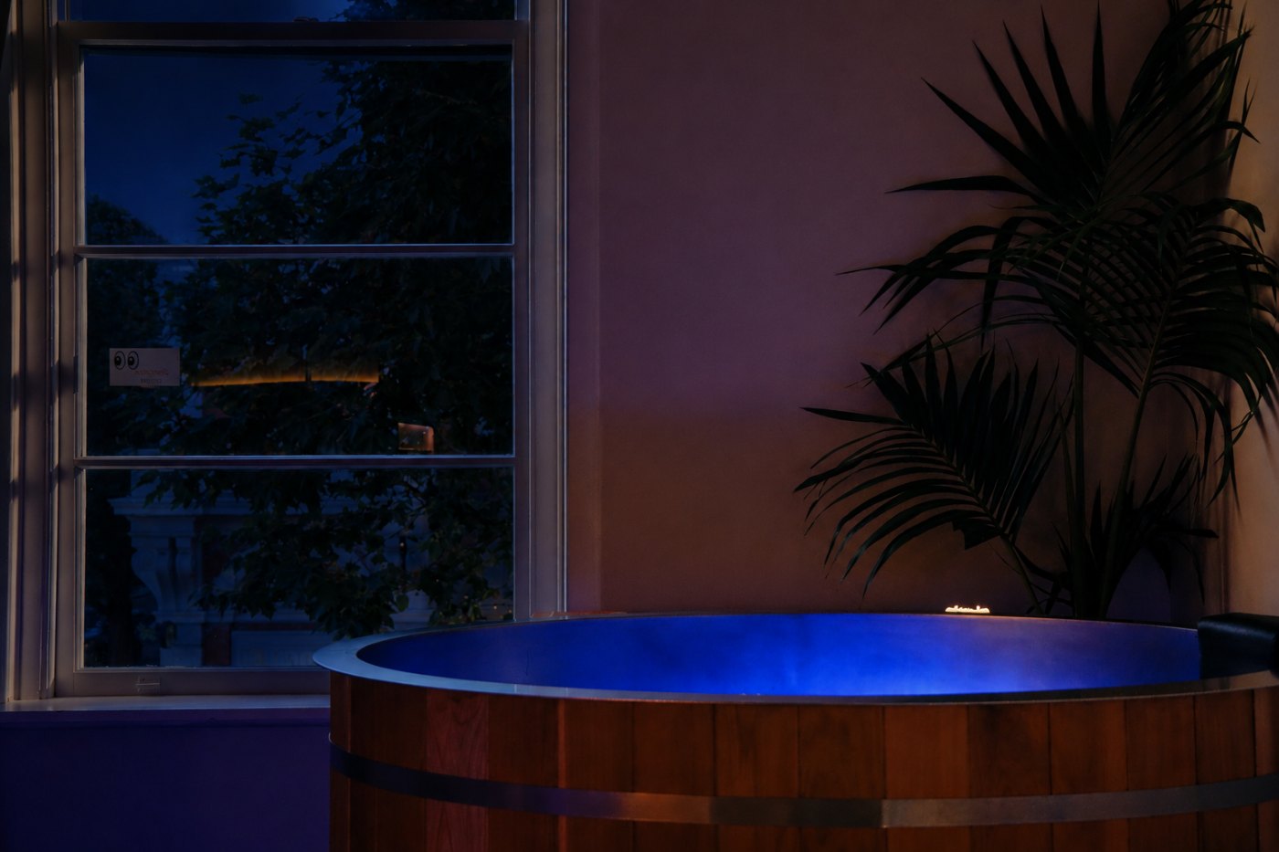Cedar cold plunge glowing blue by the window after dark