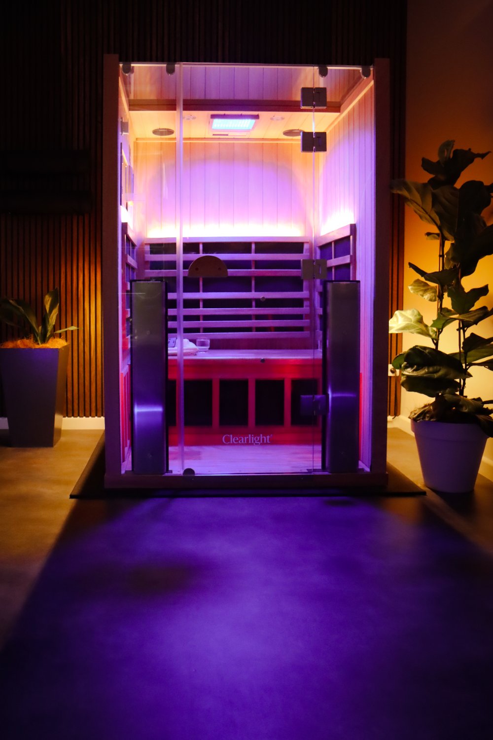 The infrared sauna glowing pink and purple beside a leafy plant
