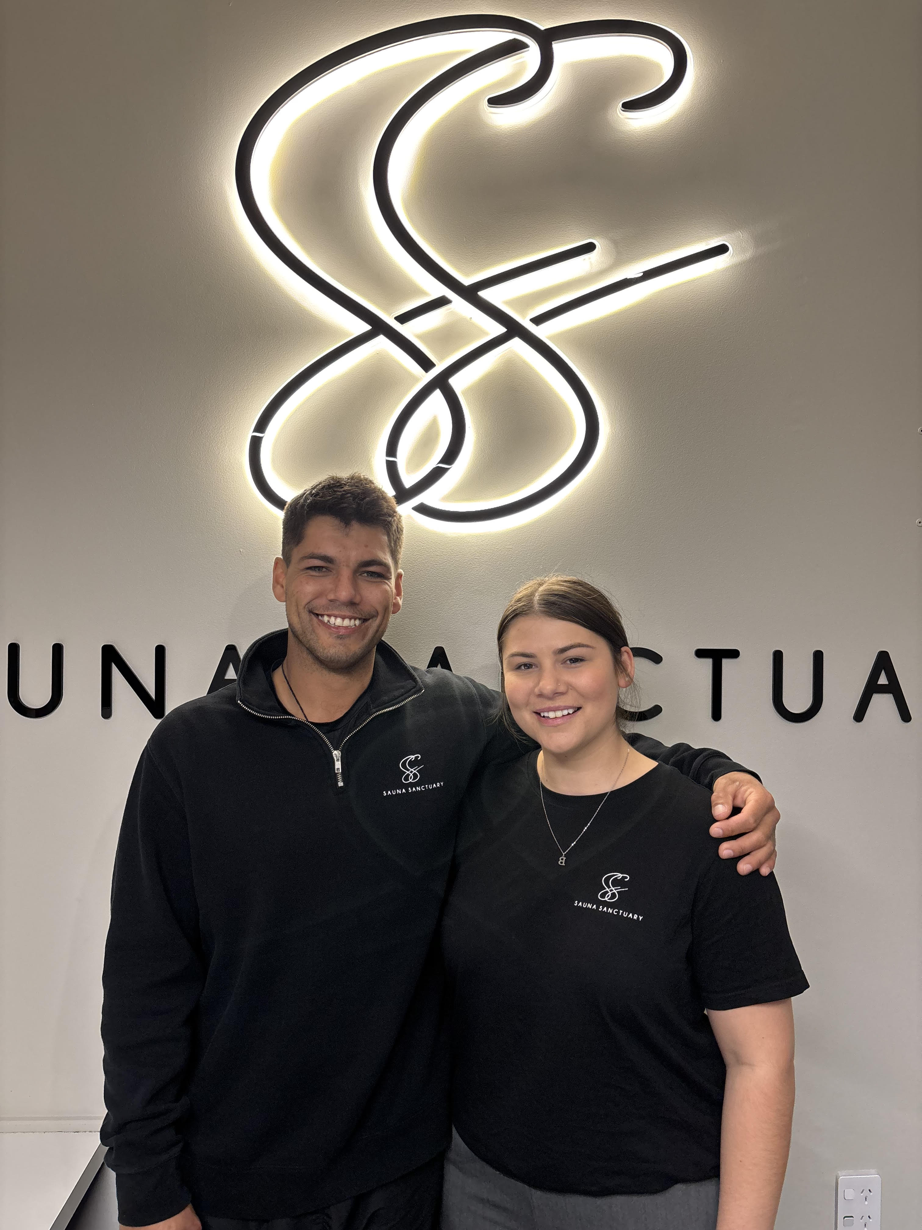 The Sauna Sanctuary team in front of the studio's illuminated logo